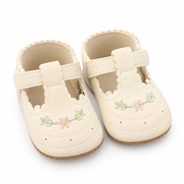 A pair of cream-colored baby Mary Jane shoes with delicate floral embroidery on the toe area, displayed on a clean white background.