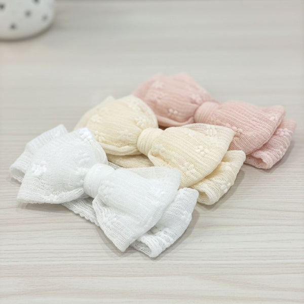 Set of folded baby blankets in white, pink, and cream on a light surface.