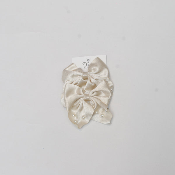 Set of cream-colored hair scrunchies with pearl embellishments on a gray background