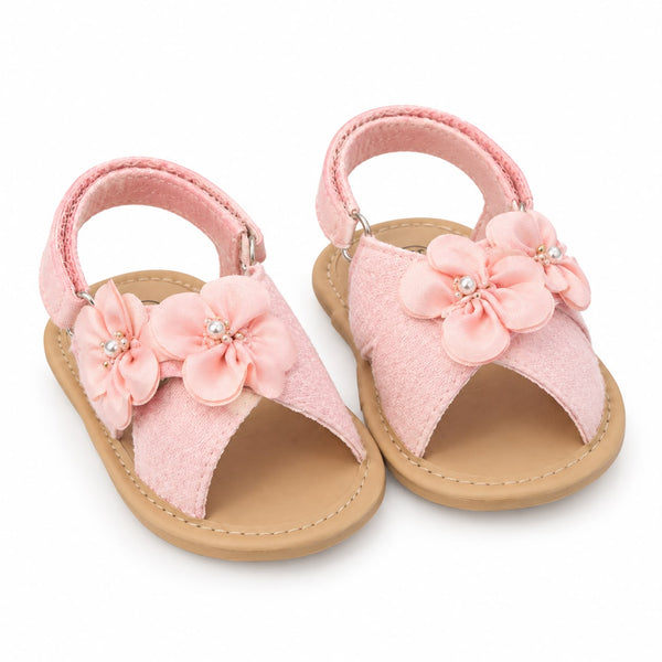 A pair of toddler open-toe sandals in light pink, featuring fabric flower embellishments on the straps and a natural tan footbed and sole, shown on a white background.