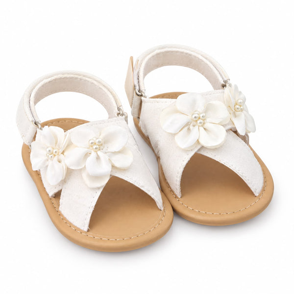 A pair of baby sandals in off-white faux leather with decorative fabric flowers and pearl-like center details, featuring tan soles, shown on a white background.