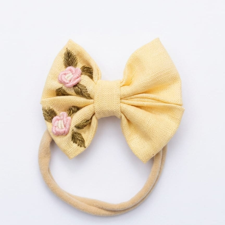 Yellow bow headband with floral embroidery on a white background