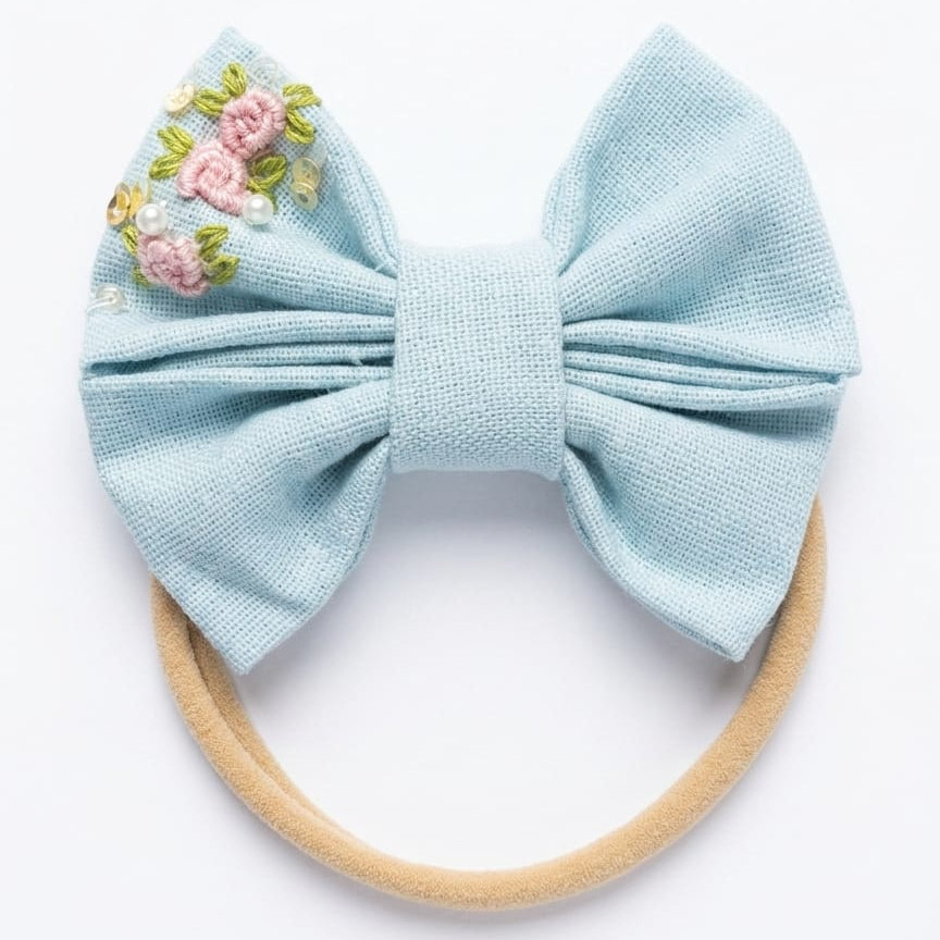 Light blue bow hair accessory with floral embroidery on a white background
