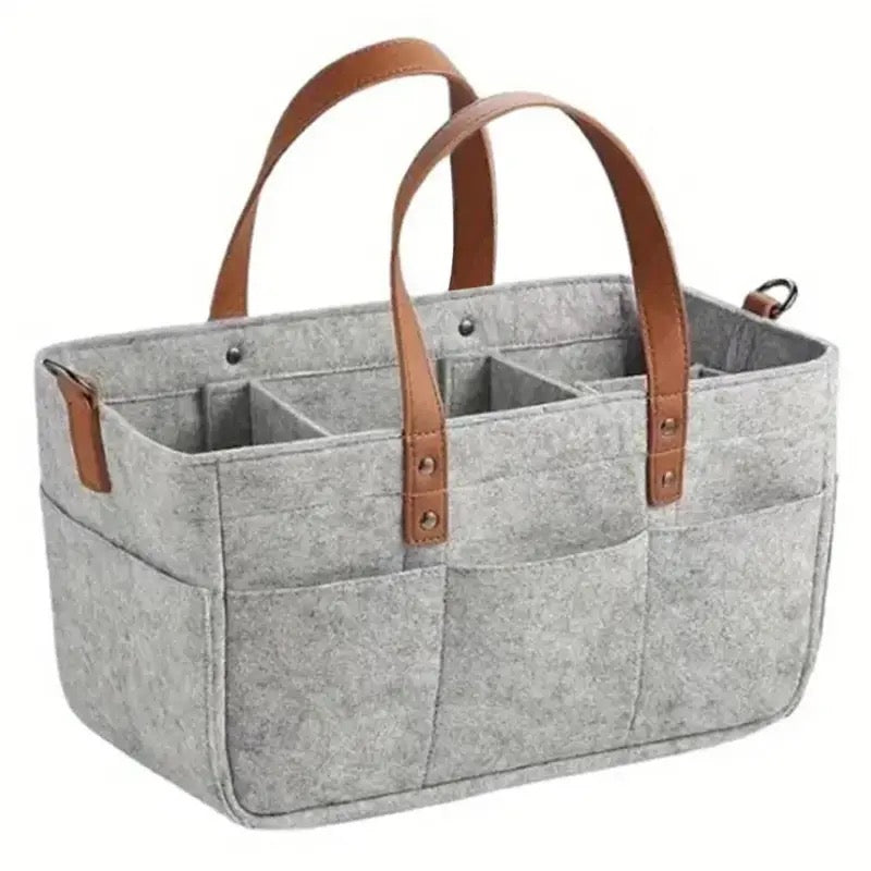 A light grey felt organizer with brown leather handles and multiple outer pockets, designed for diaper storage but versatile for other uses.