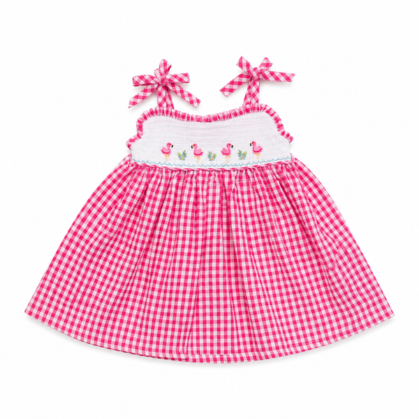 A pink and white gingham baby dress with a smocked white chest panel featuring embroidered pink flamingos and small green leaves. The dress has ruffled shoulder straps that tie into matching pink and white gingham bows, shown against a plain white background.