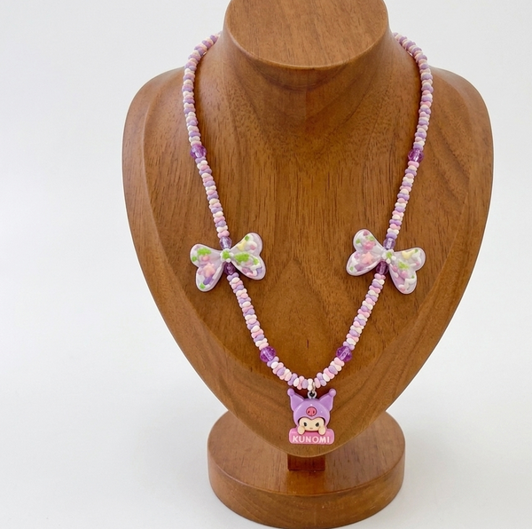 A pink beaded necklace with butterfly charms and a small cartoon character pendant, displayed on a wooden jewelry bust against a white background.