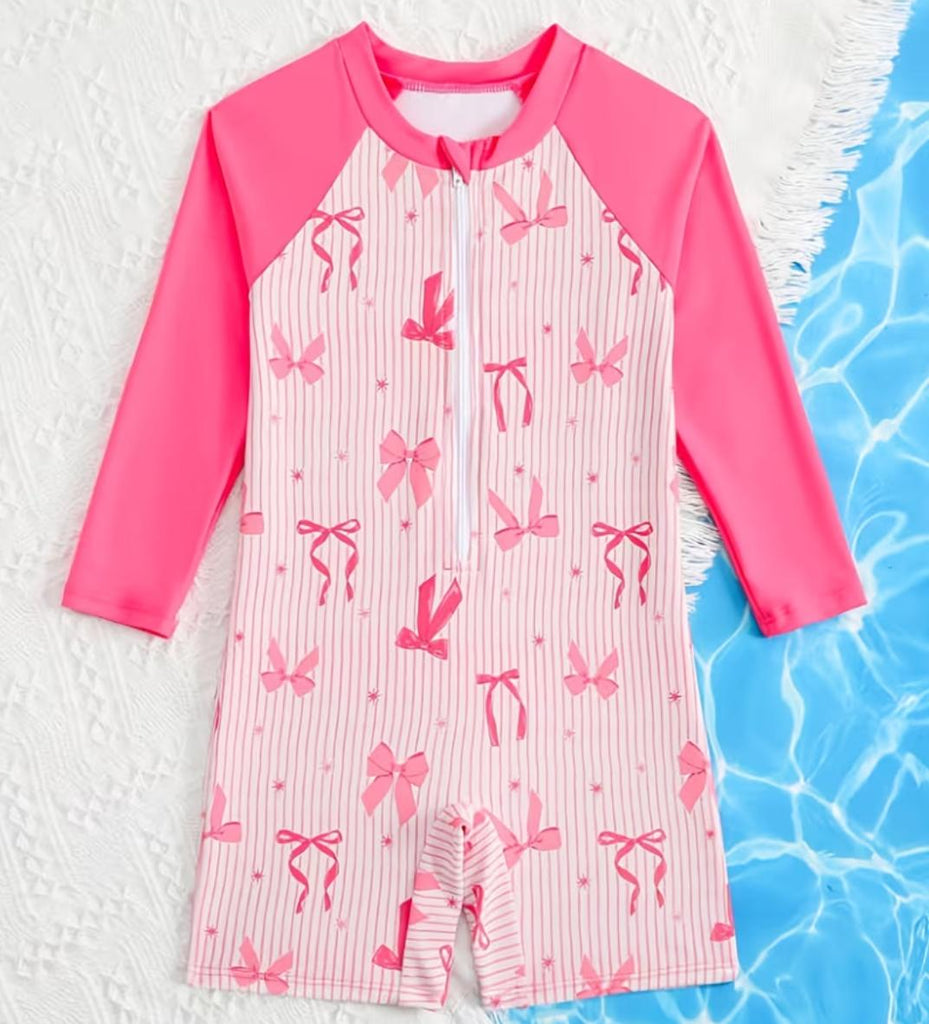Pink and white children's swimsuit with bow pattern on a textured surface.