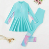 A long sleeve rash guard for girls with a zipper front, presented in a teal color with matching teal and patterned swim leggings.