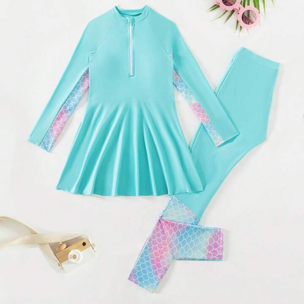 A long sleeve rash guard for girls with a zipper front, presented in a teal color with matching teal and patterned swim leggings.