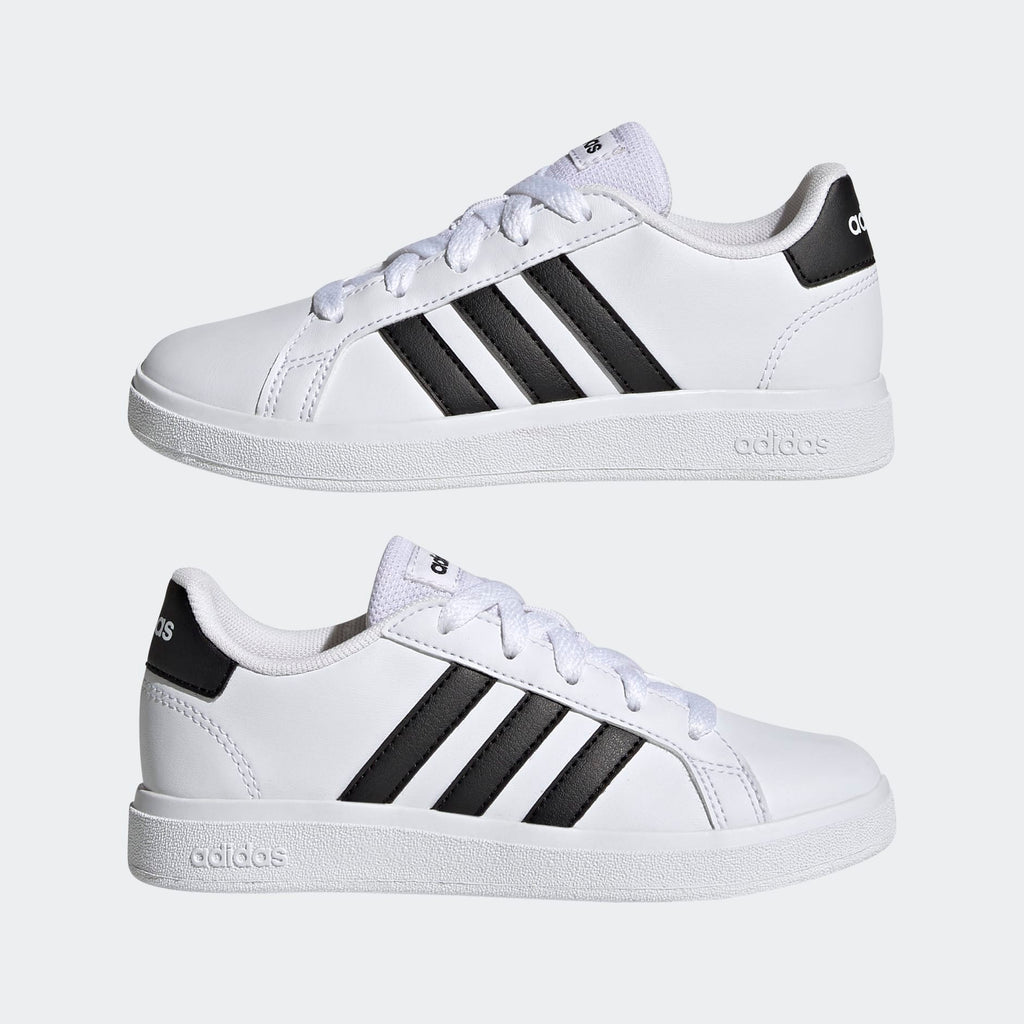 A pair of white Adidas Grand Court Lifestyle Tennis lace-up shoes for kids with black stripes and brand logo on the side.