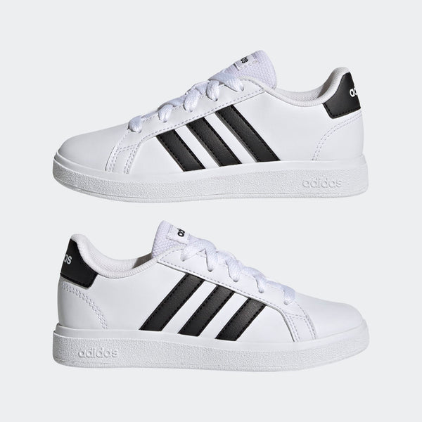 A pair of white Adidas Grand Court Lifestyle Tennis lace-up shoes for kids with black stripes and brand logo on the side.