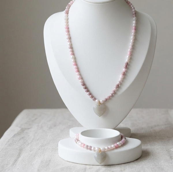 A pink beaded necklace and matching bracelet displayed on a white jewelry bust against a soft neutral background.