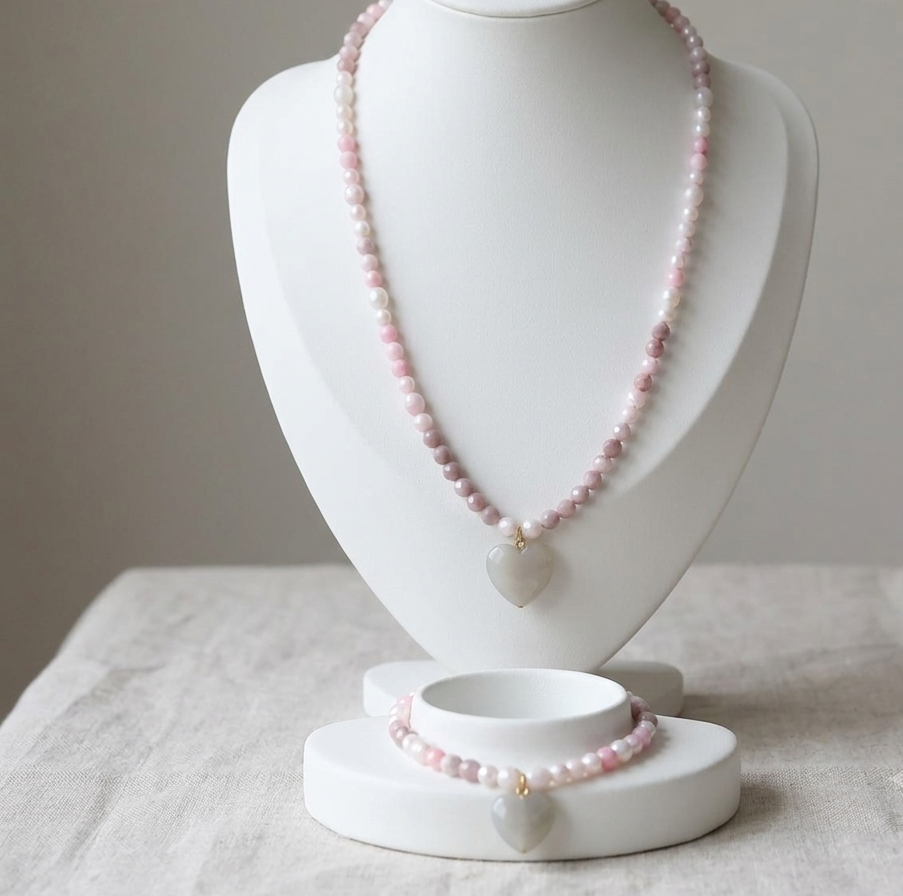 A pink beaded necklace and matching bracelet displayed on a white jewelry bust against a soft neutral background.