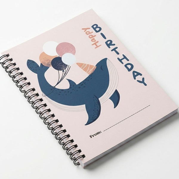 Notebook with a whale illustration and 'Happy Birthday' text on a pink background