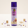 Disney Princess Rapunzel hair and body spray bottle in purple, surrounded by decorative gold star-shaped accessories, small purple flowers, and lavender petals on a clean off-white background.