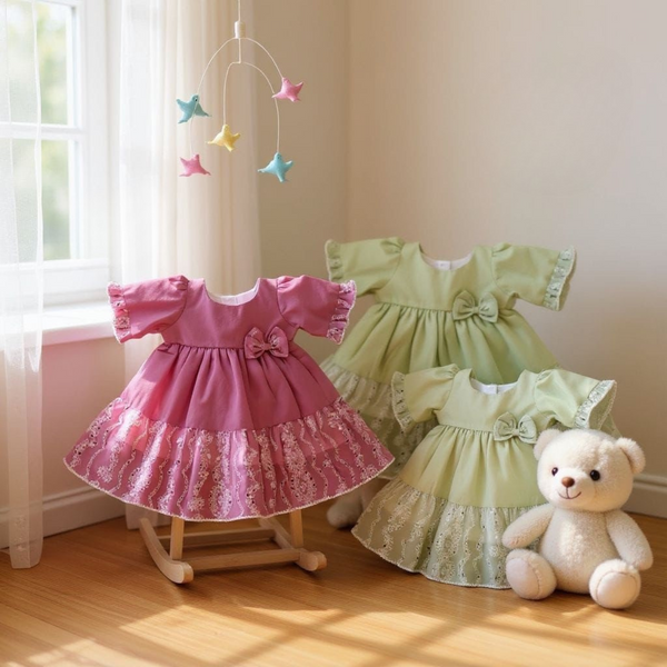Two children's dresses in pink and green with a teddy bear and star mobile in a nursery.