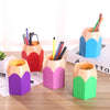 Colorful pencil-shaped pen holders with pens on a wooden surface.