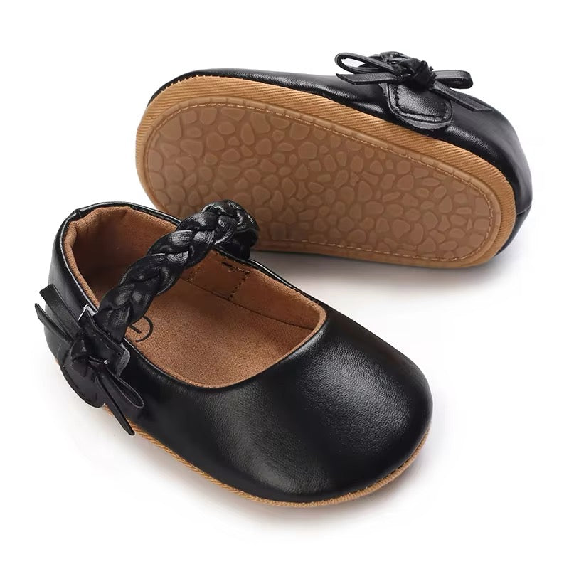 A pair of black baby shoes with braided details and a velcro strap, designed for infant feet.