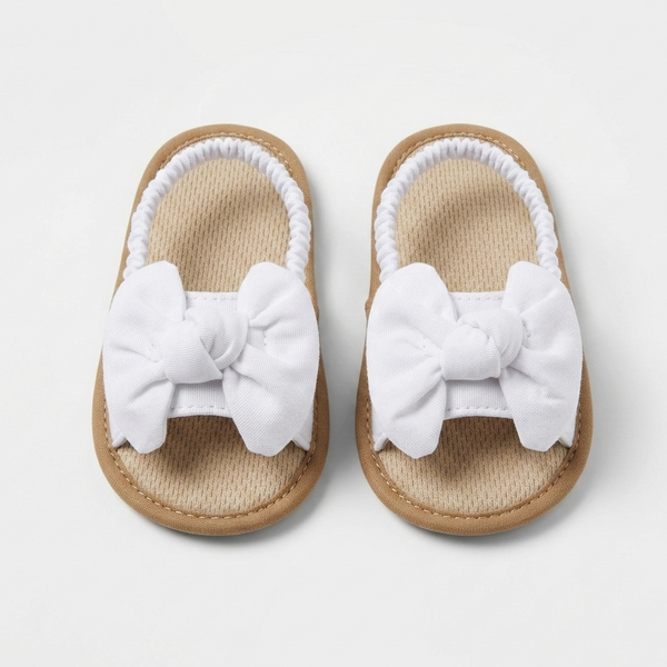 Pair of baby girl sandals with white bows on a light gray background