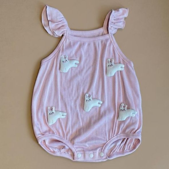 Pink baby romper with bunny designs on a beige background