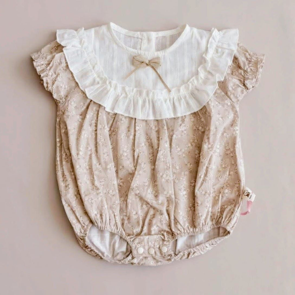 Baby romper with lace collar and bow on a light pink background