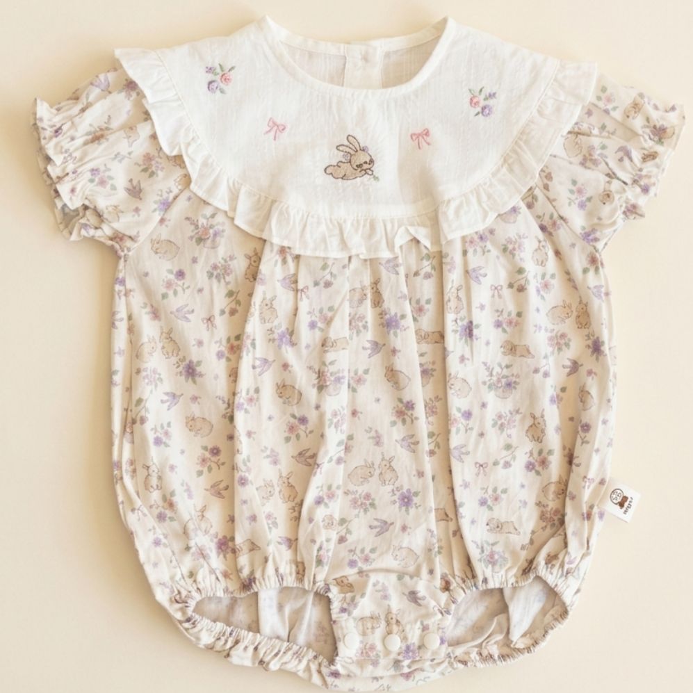 Floral baby romper with ruffled collar on a beige background