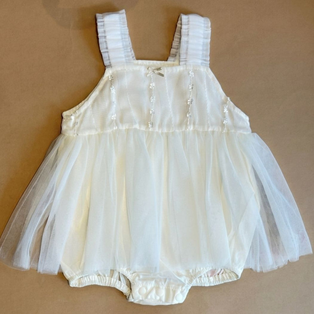 White baby romper with lace details on a beige background