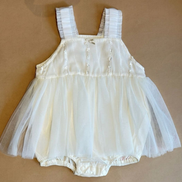 White baby romper with lace details on a beige background