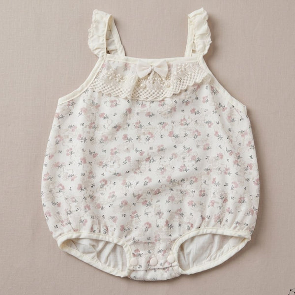 Floral baby romper with lace details on a beige background