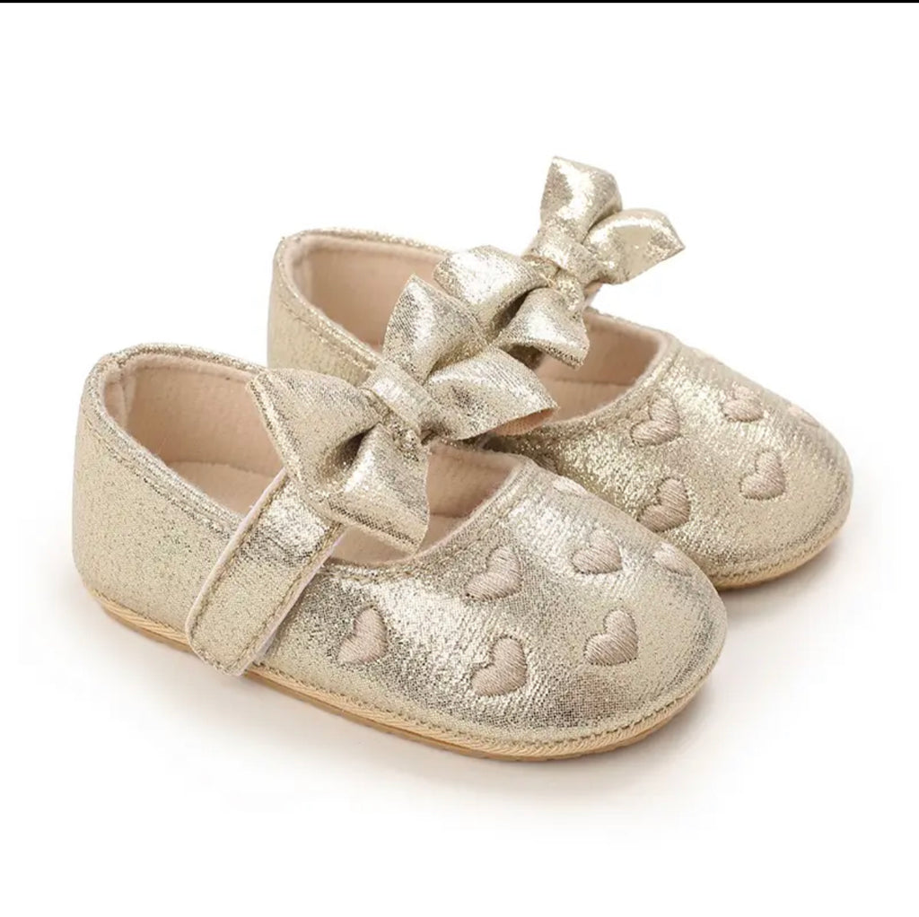 A pair of gold baby shoes with a soft bow and heart patterns.