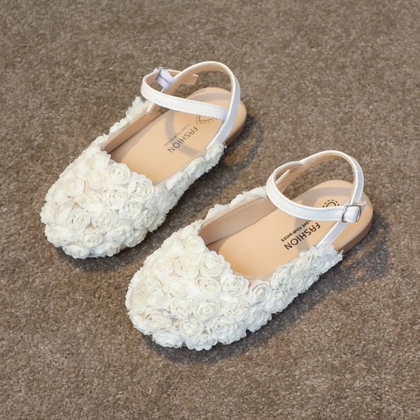 A pair of white toddler shoes with floral rosette design and hook and loop closures on a grey background.