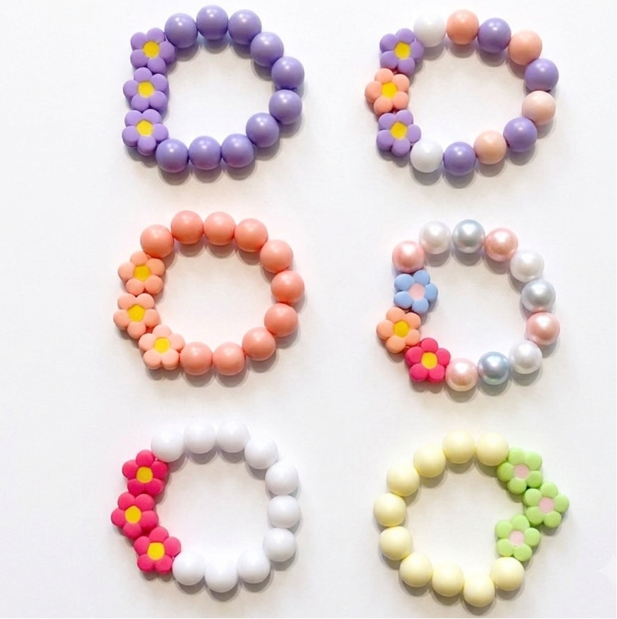 Six pastel bead bracelets arranged in a 3-by-2 grid on a white background. The bracelets feature various pastel colors including purple, peach, pink, white, yellow, and green, with two designs incorporating small flower charms with yellow centers.
