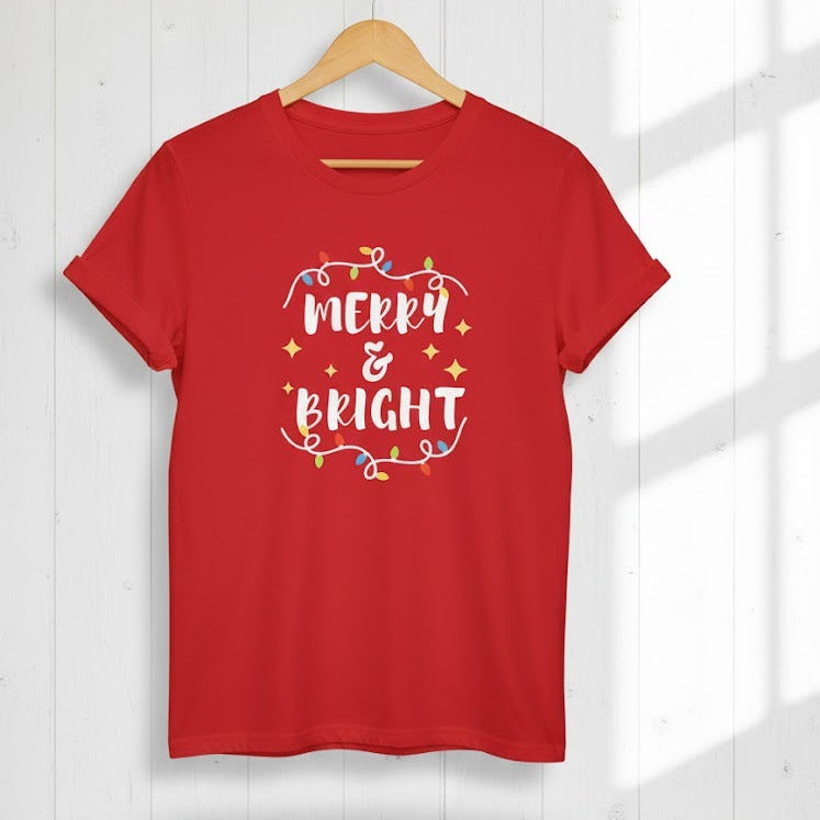 Red t-shirt with 'Merry & Bright' text on a hanger against a white wall.
