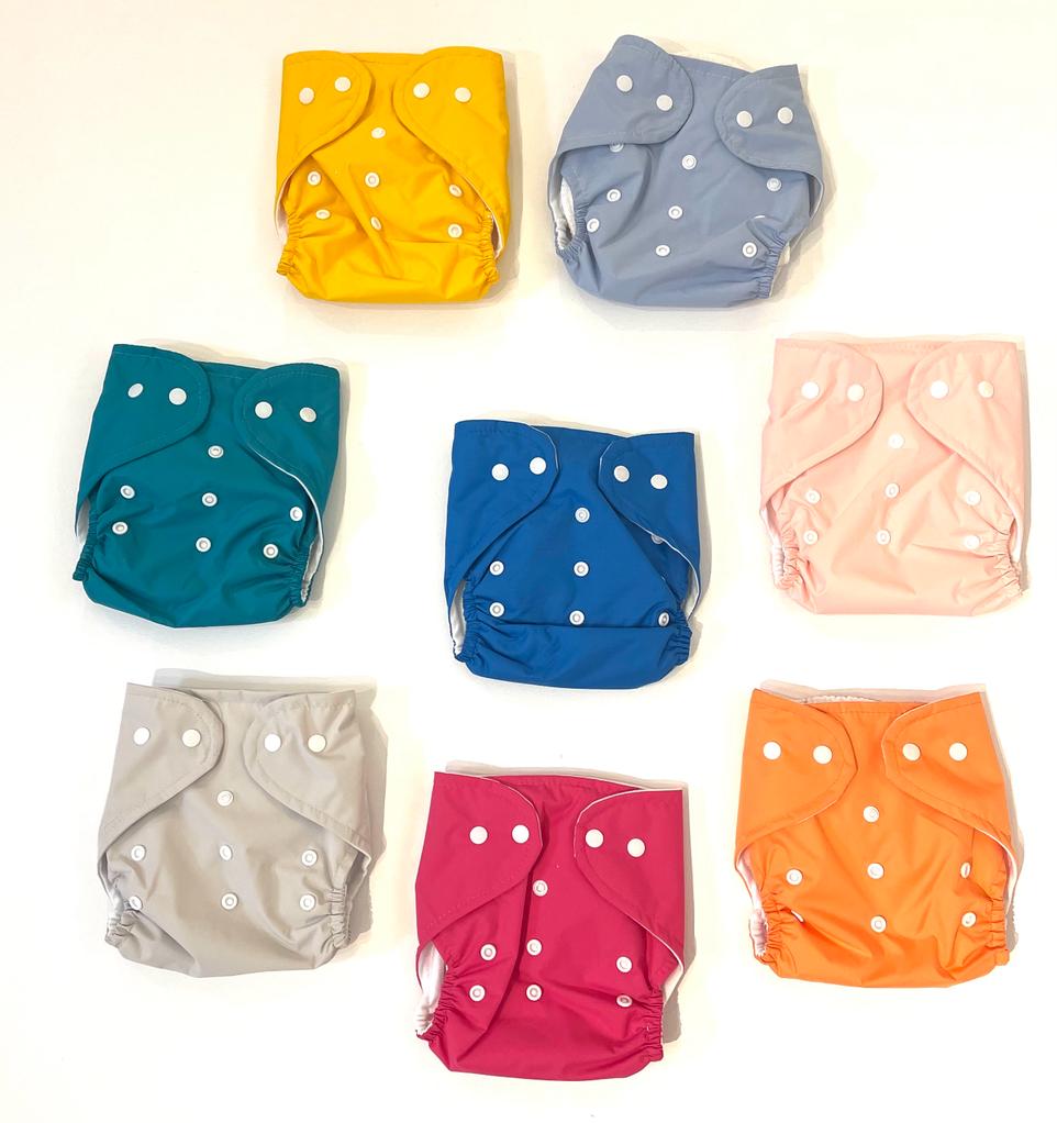 A collection of diapers in various colors, each with a padded insert visible. The colors include yellow, blue, gray, pink, and orange, all with a dotted pattern and snaps on the wings.