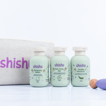 Three small travel-sized baby care bottles with labels, arranged in front of a light-colored bag with the brand name visible.