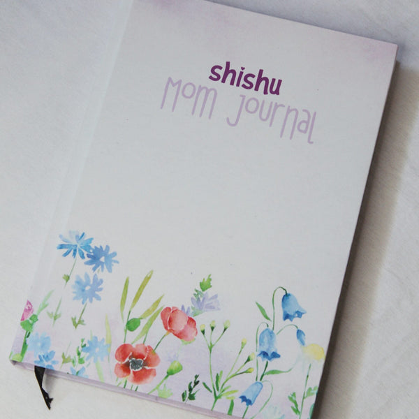 A photo of a 'Shishu Mom Journal' with a floral design on the cover in watercolor style.