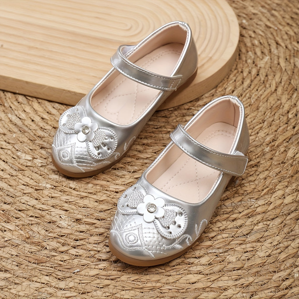 Pair of silver children's shoes with floral designs on a woven mat