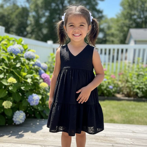 Young girl in a black dress standing outdoors with flowers and a white fence in the background