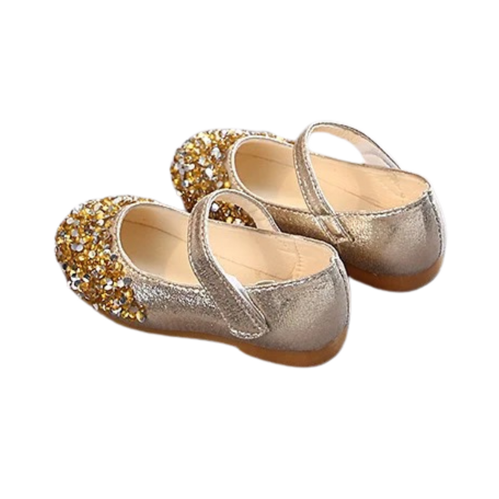 A pair of toddler-sized sparkly party shoes with gold and silver colors, featuring a flat sole and decorative glitter on the top.