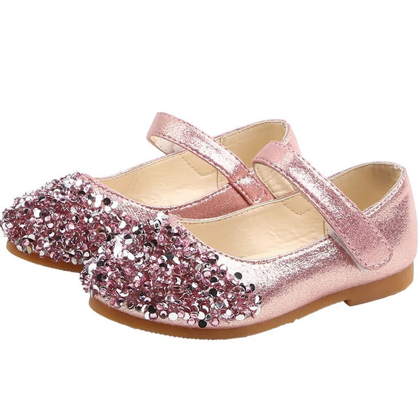 A pair of pink sparkly party shoes for toddlers with a bow and rhinestone embellishments.