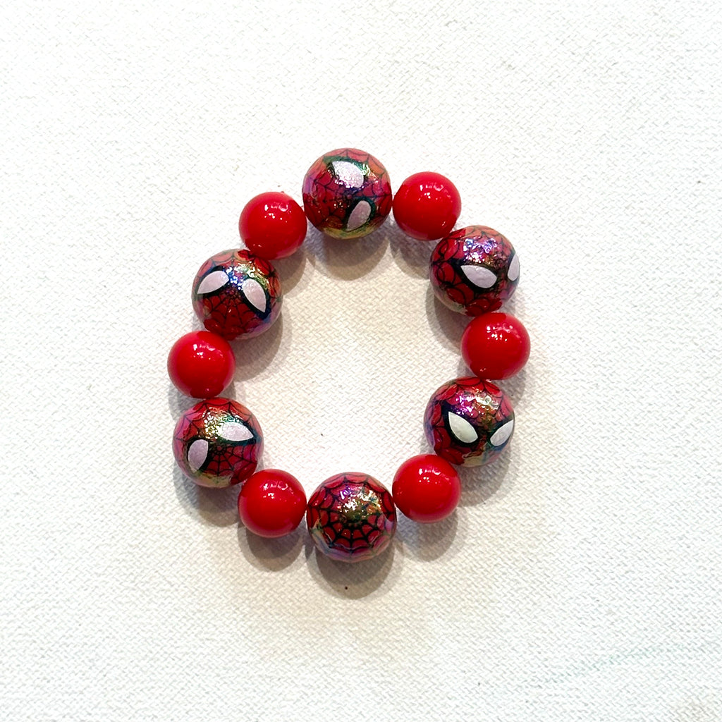 A beaded stretch bracelet featuring alternating solid red beads and spider-themed glass beads with a red and black web pattern and white spider eyes, displayed on a textured white fabric background.