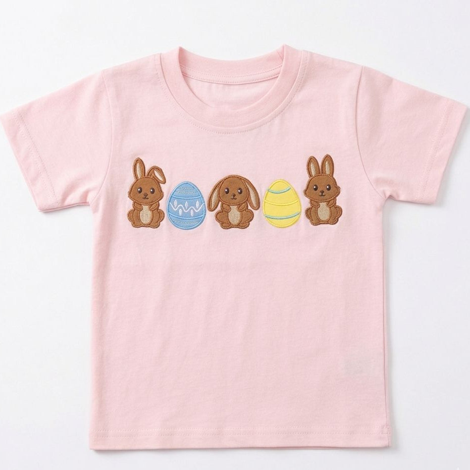 Pink t-shirt with Easter-themed design featuring bunnies and eggs on a white background