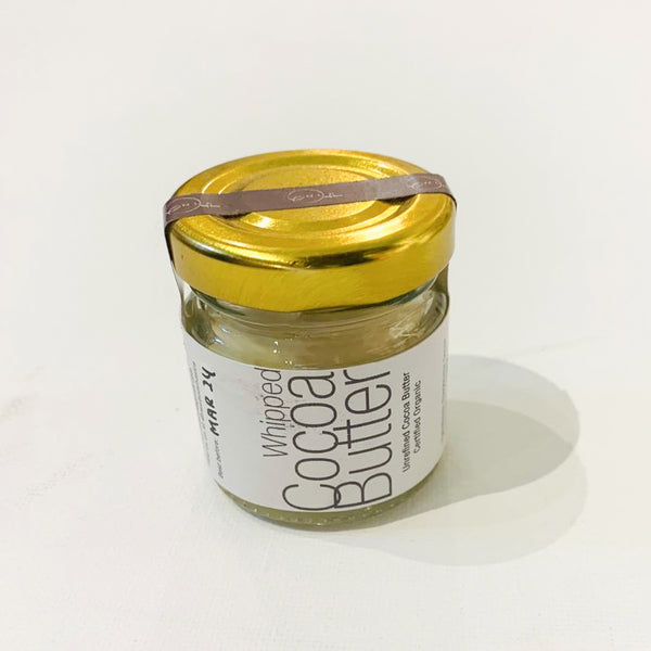 A jar of Whipped Cocoa Butter with Vitamin E by Nue Body Basics, with a label that includes the product name and the statement 'Free from synthetic fragrances'. The jar is sealed with a brown lid and placed on a white background.