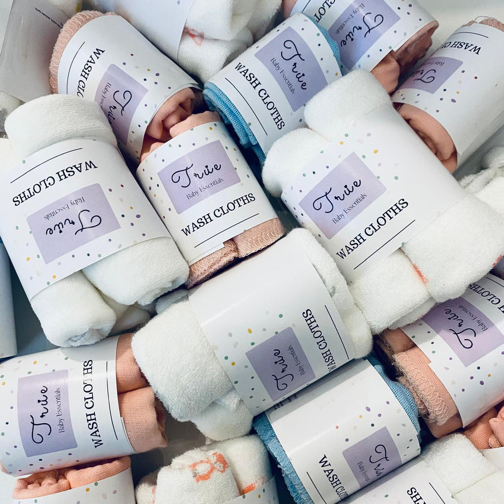 A collection of folded wash cloths in various colors, each with a label indicating the brand 'True' and the product type 'Wash Cloths'. The cloths are stacked in a pile, with some multicolored cloths visible at the bottom.