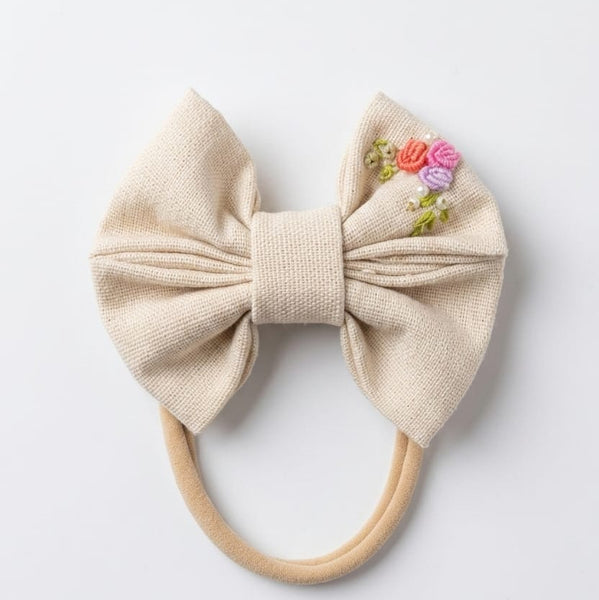 Beige bow hair accessory with floral embellishments on a white background