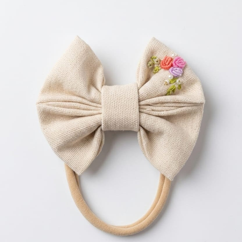 Beige bow hair accessory with floral embellishments on a white background