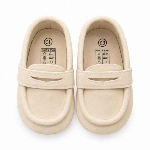 A pair of cream-colored baby loafers with a single strap across the top, photographed from a top-down view on a white background.