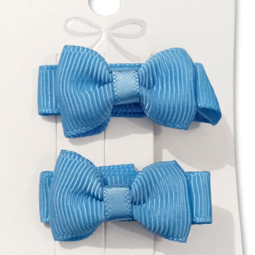 Two blue hair bows on a white card with a decorative bow design.