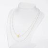 A double-strand pearl necklace with a small white daisy pendant featuring a yellow center, displayed on a clear acrylic jewelry bust against a white background.