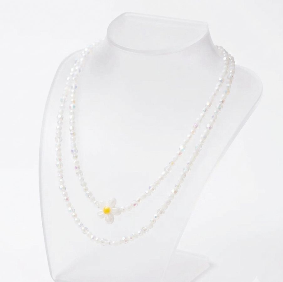 A double-strand pearl necklace with a small white daisy pendant featuring a yellow center, displayed on a clear acrylic jewelry bust against a white background.